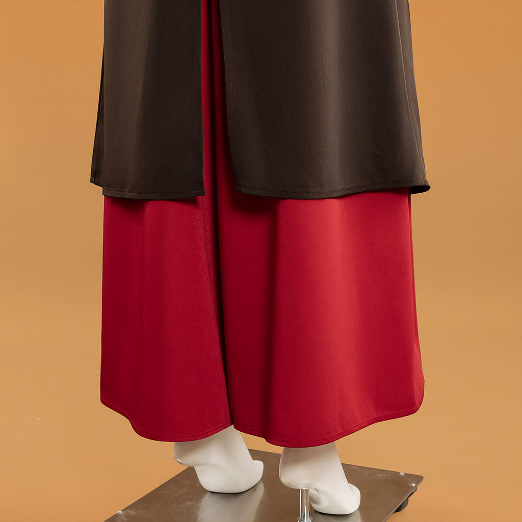 Rear hem detail of the Mai red trousers beneath the dark outer layer