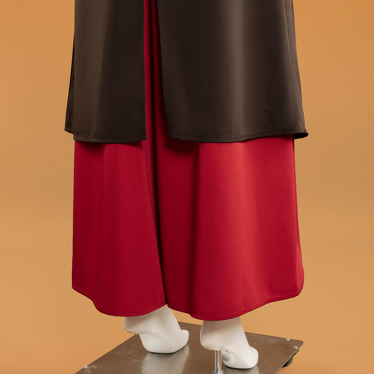 Rear hem detail of the Mai red trousers beneath the dark outer layer
